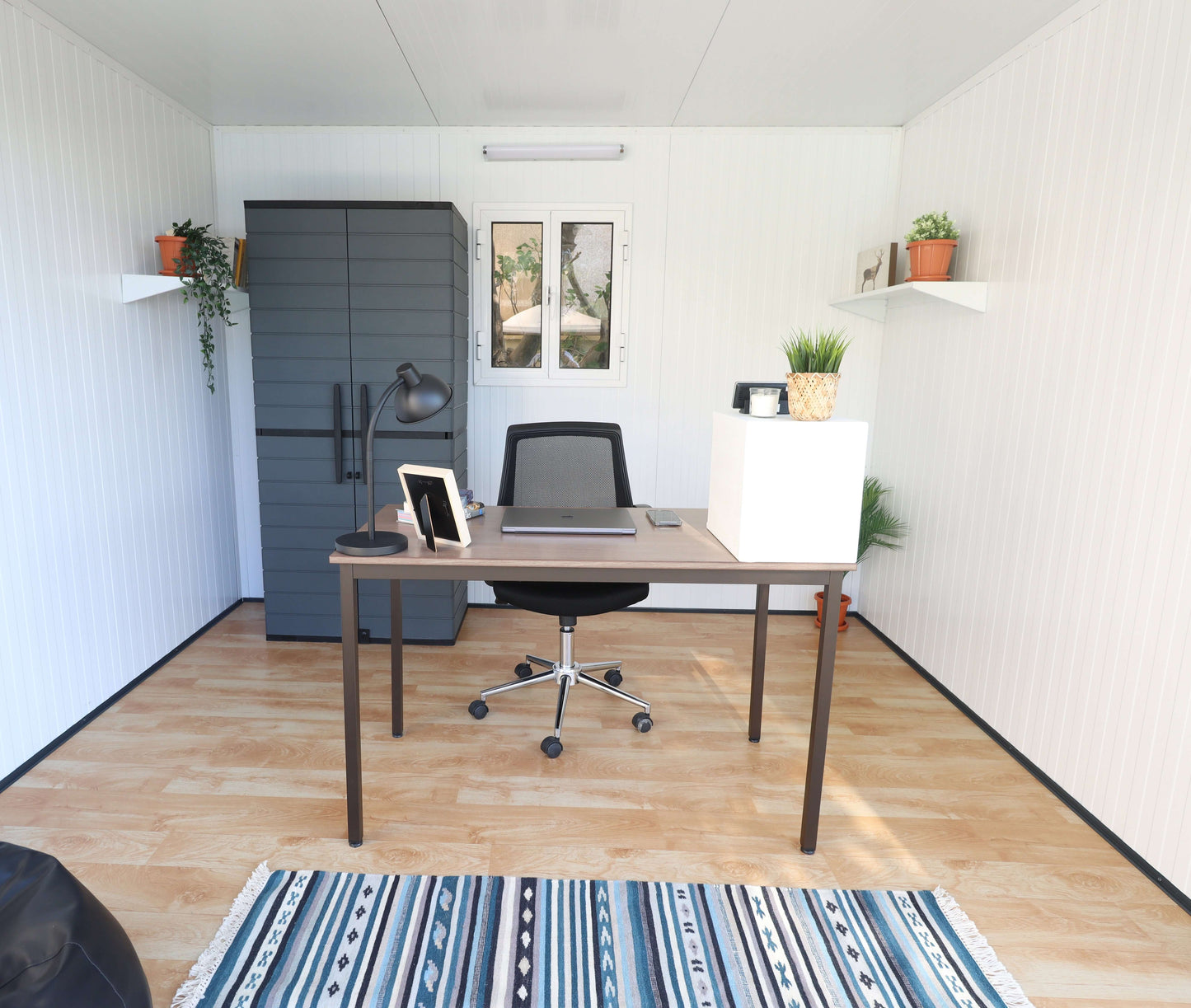 Interior of Duramax 10x10 Glass Garden Room with desk, chair, and plants, ideal as an office space. Features modern decor and ample lighting.