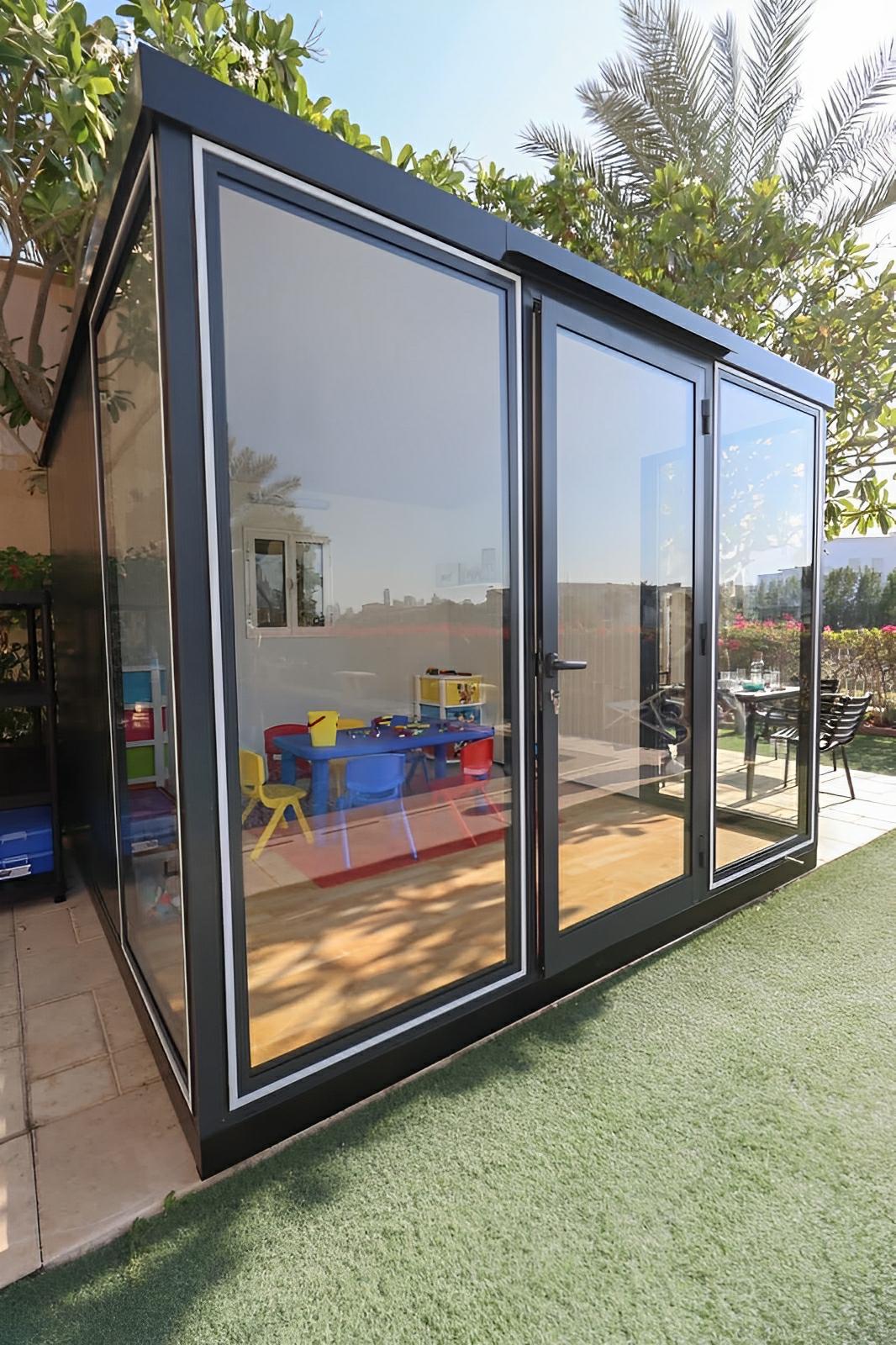 Duramax 10x10 glass garden room with steel walls and clear panels in backyard setting, used as office and playroom.