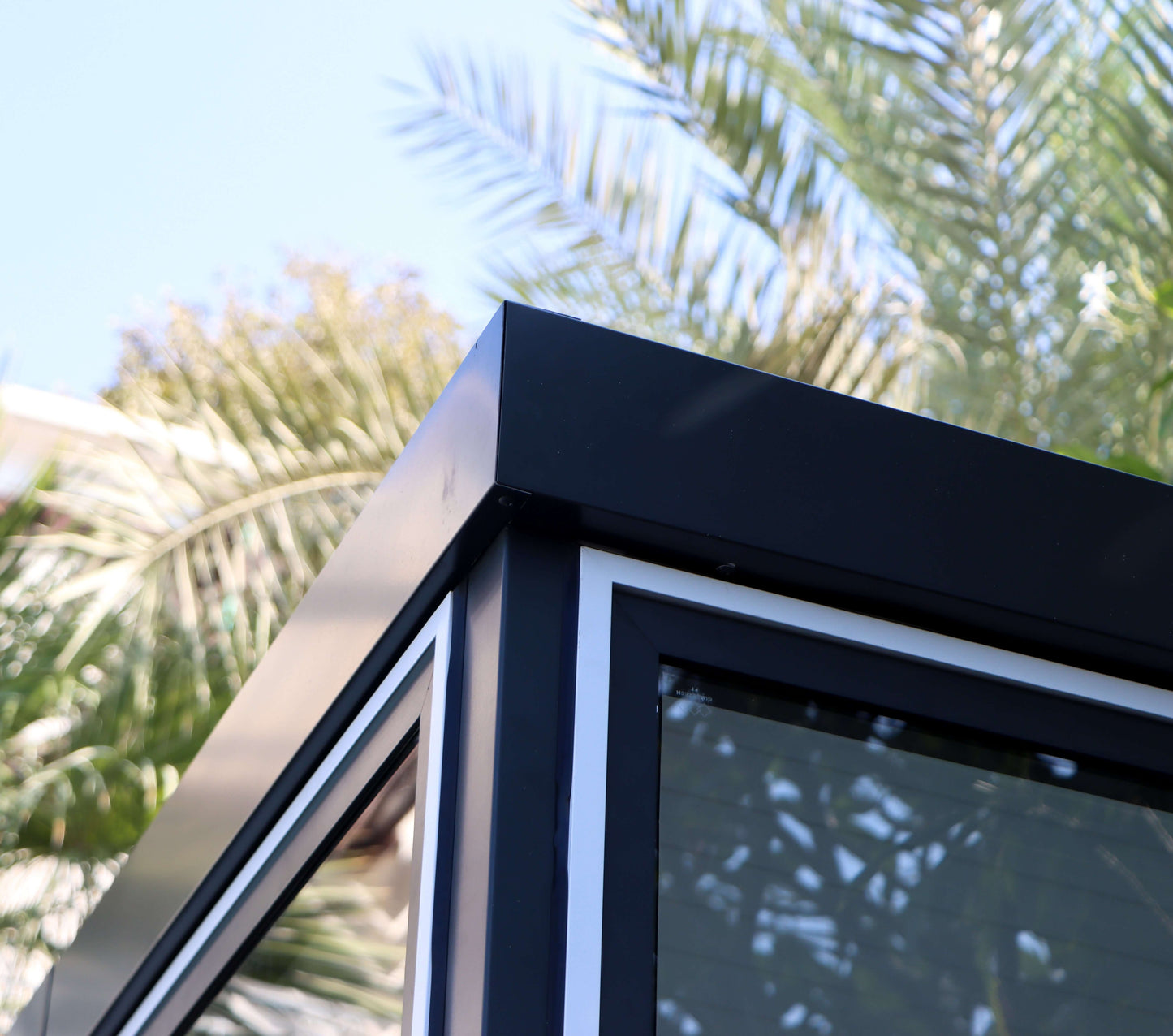 Close-up of Duramax 10x10 Glass Garden Room with sleek corner design, against a backdrop of palm trees.