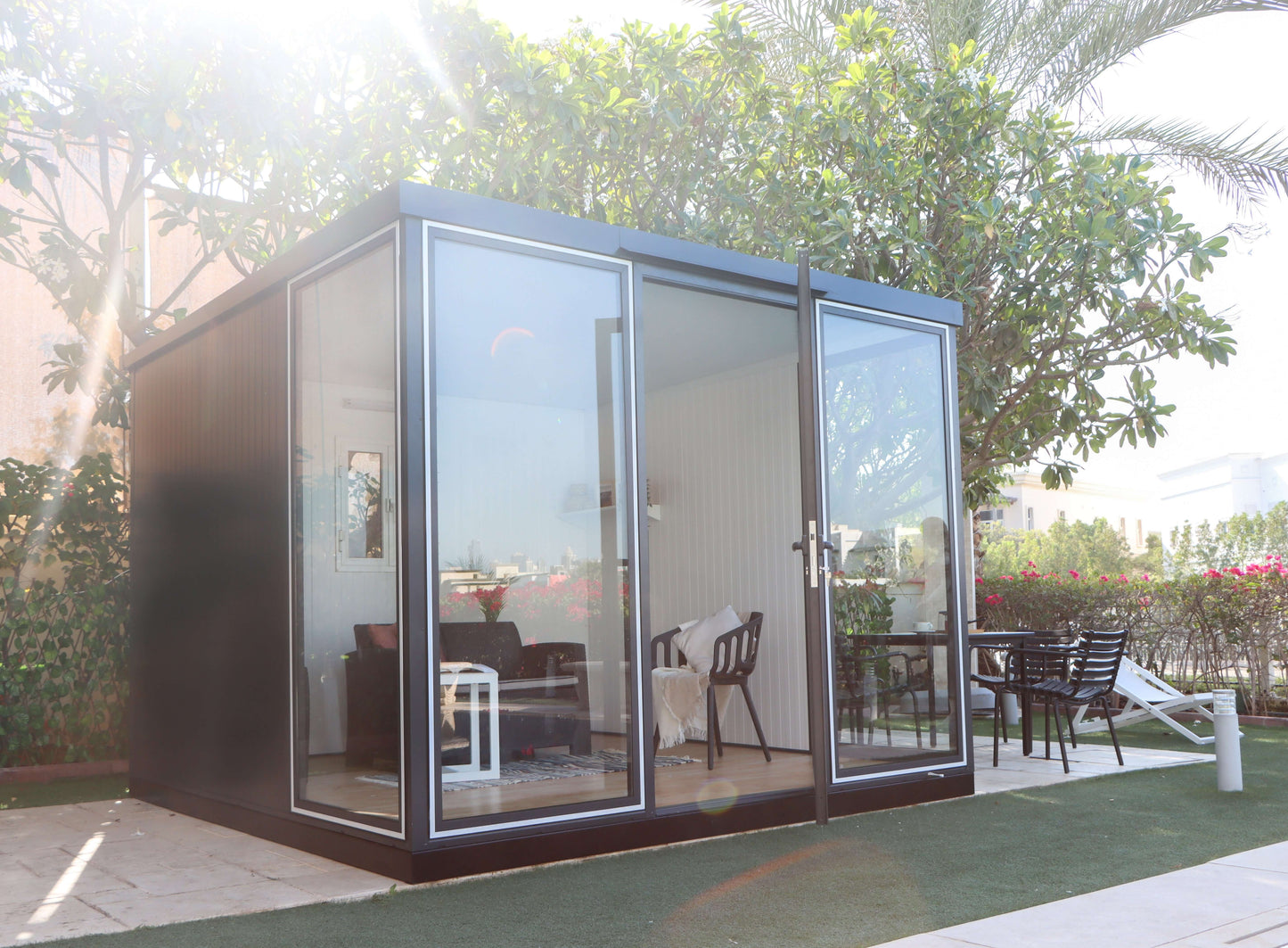 Duramax 10x10 Glass Garden Room in a backyard, ideal as a shed, office, or guest room, featuring steel walls and clear panels.