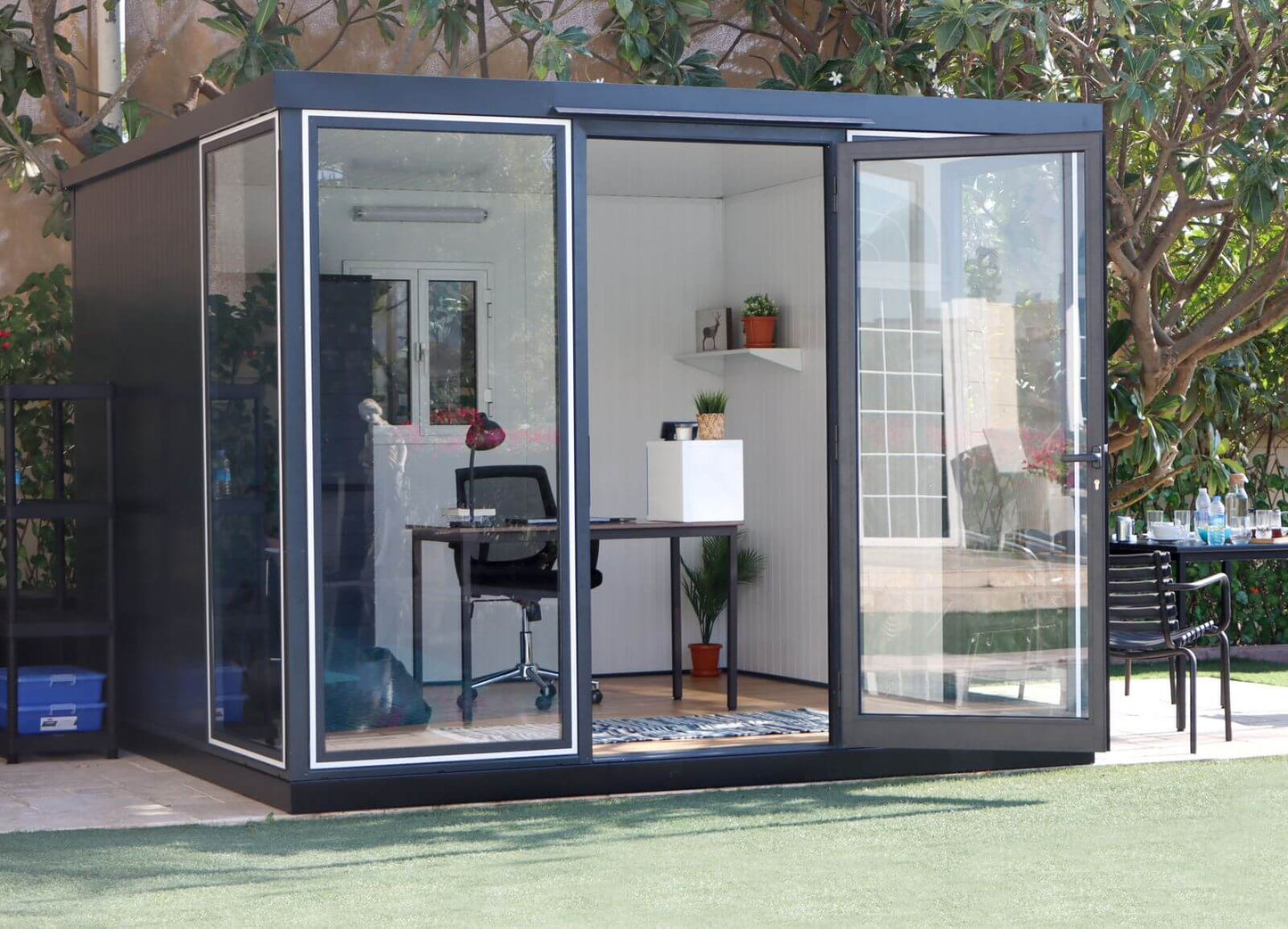 Duramax 10x10 Glass Garden Room 32001 with steel walls and clear panels, used as an office space in a backyard setting.