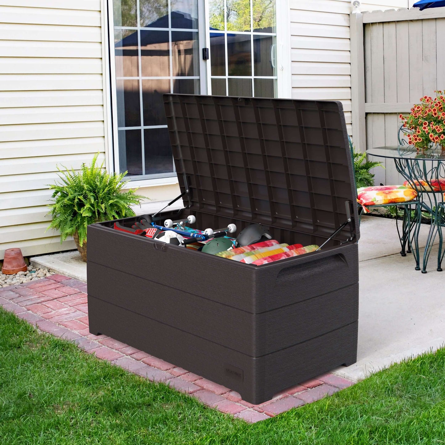 Duramax Cedar Grain Deck Box 110 Gal in brown on patio, open showing outdoor storage items, made from fire-resistant resin.