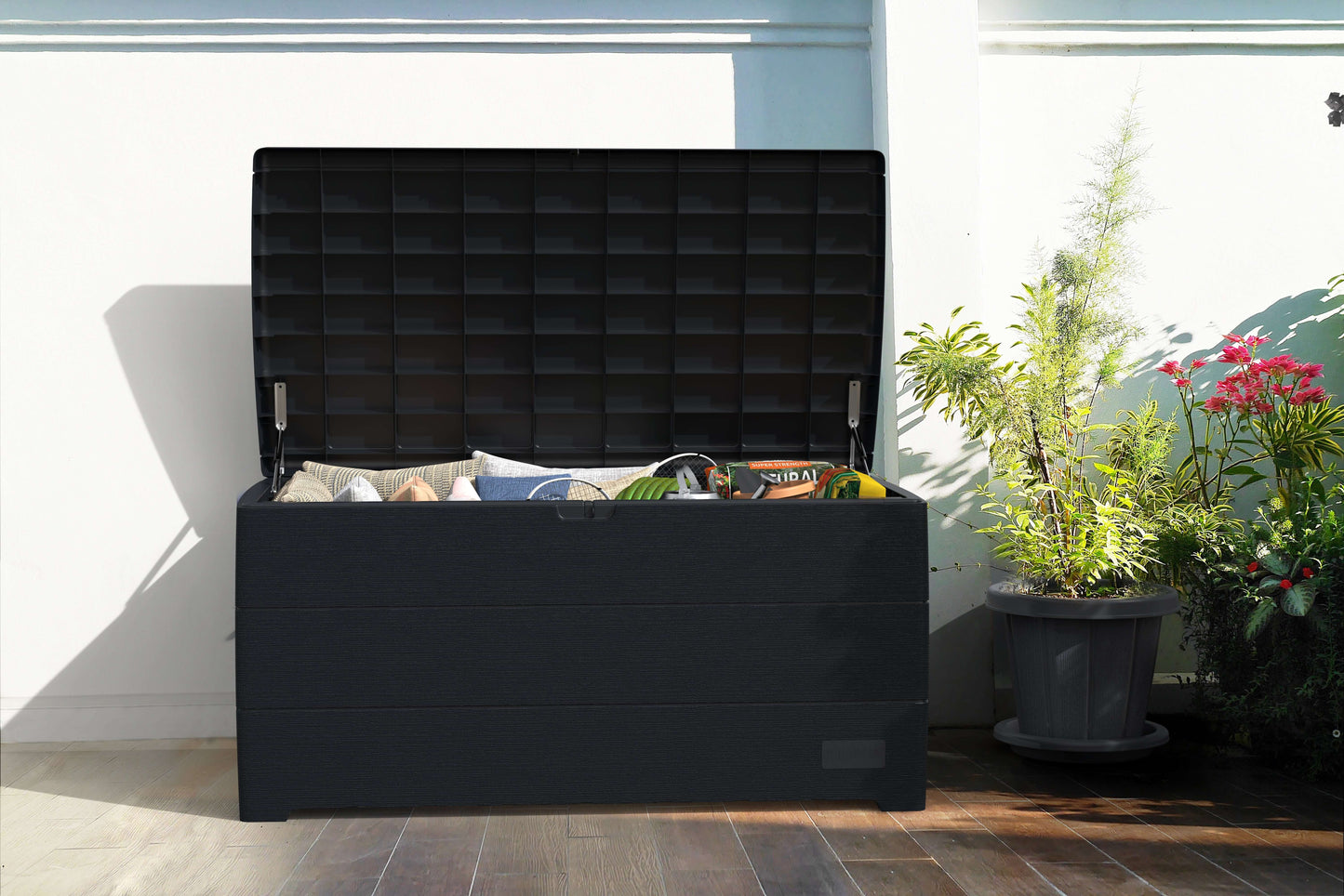 Duramax 110 Gal. CedarGrain Deck Box in gray on patio, open and storing outdoor items, surrounded by plants.