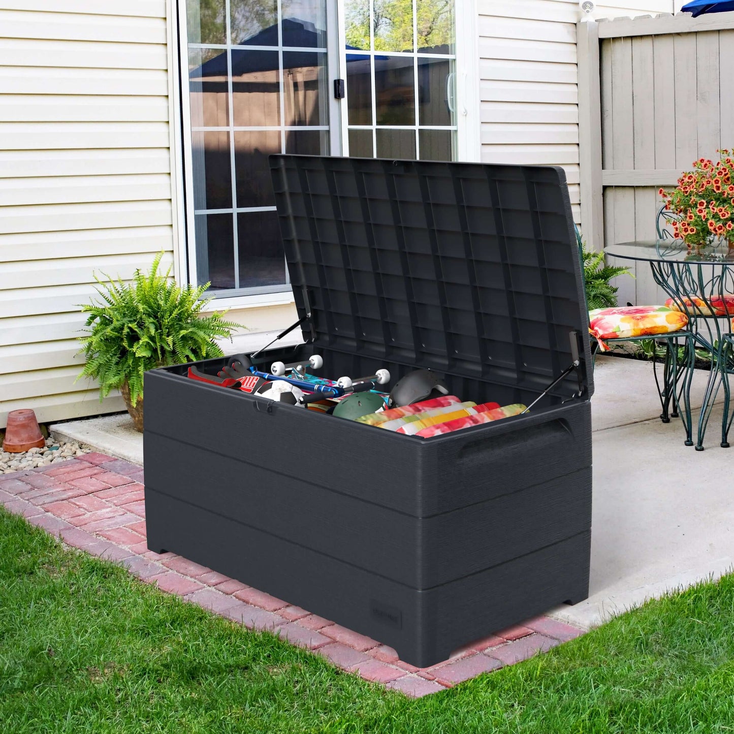 Duramax 110 Gal. Cedar Grain Deck Box in gray, open with stored items, placed on a patio, showcasing durable outdoor storage solution.