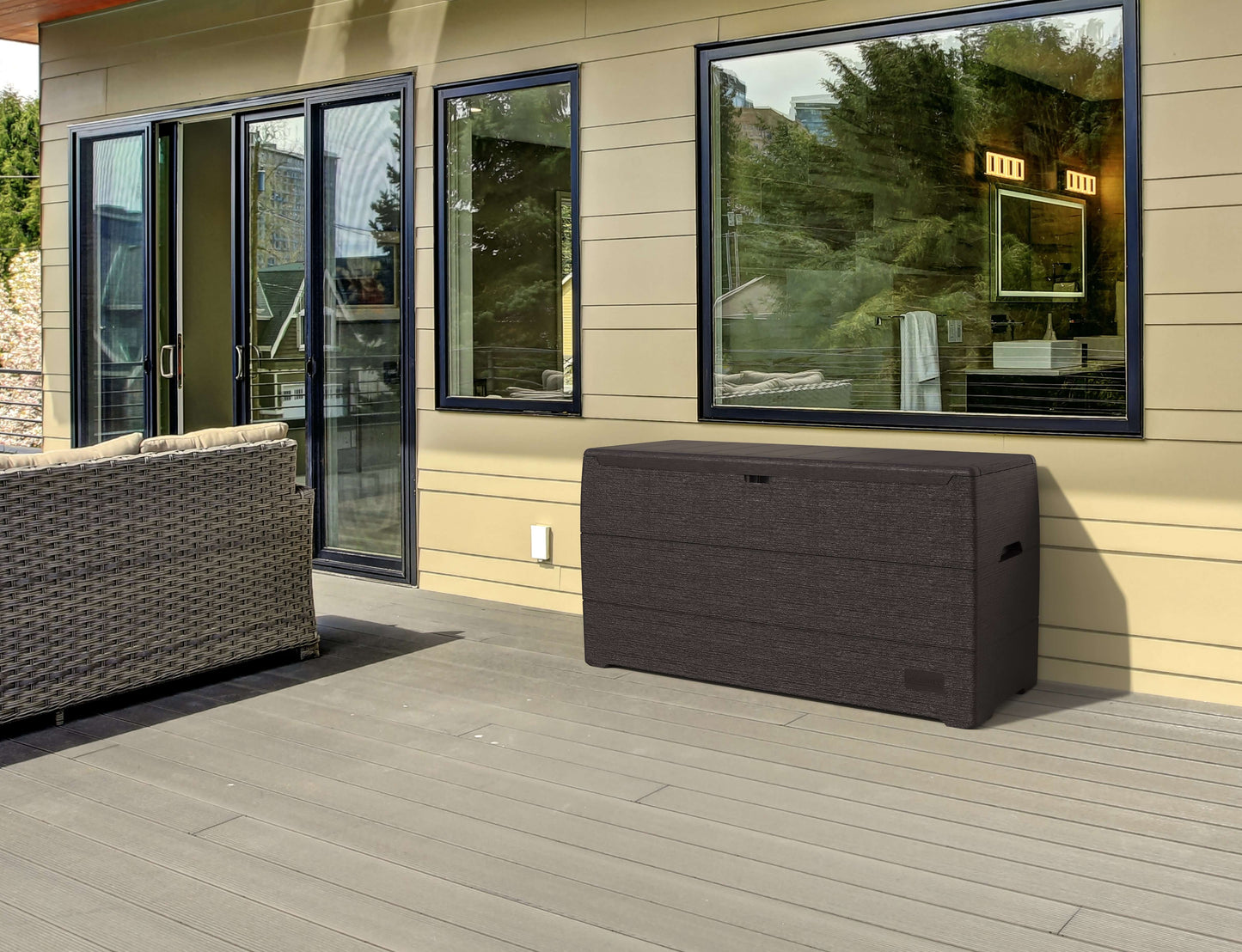 Duramax 71 Gallon Deck Box in brown with glass window reflection on patio, ideal for outdoor storage and seating.