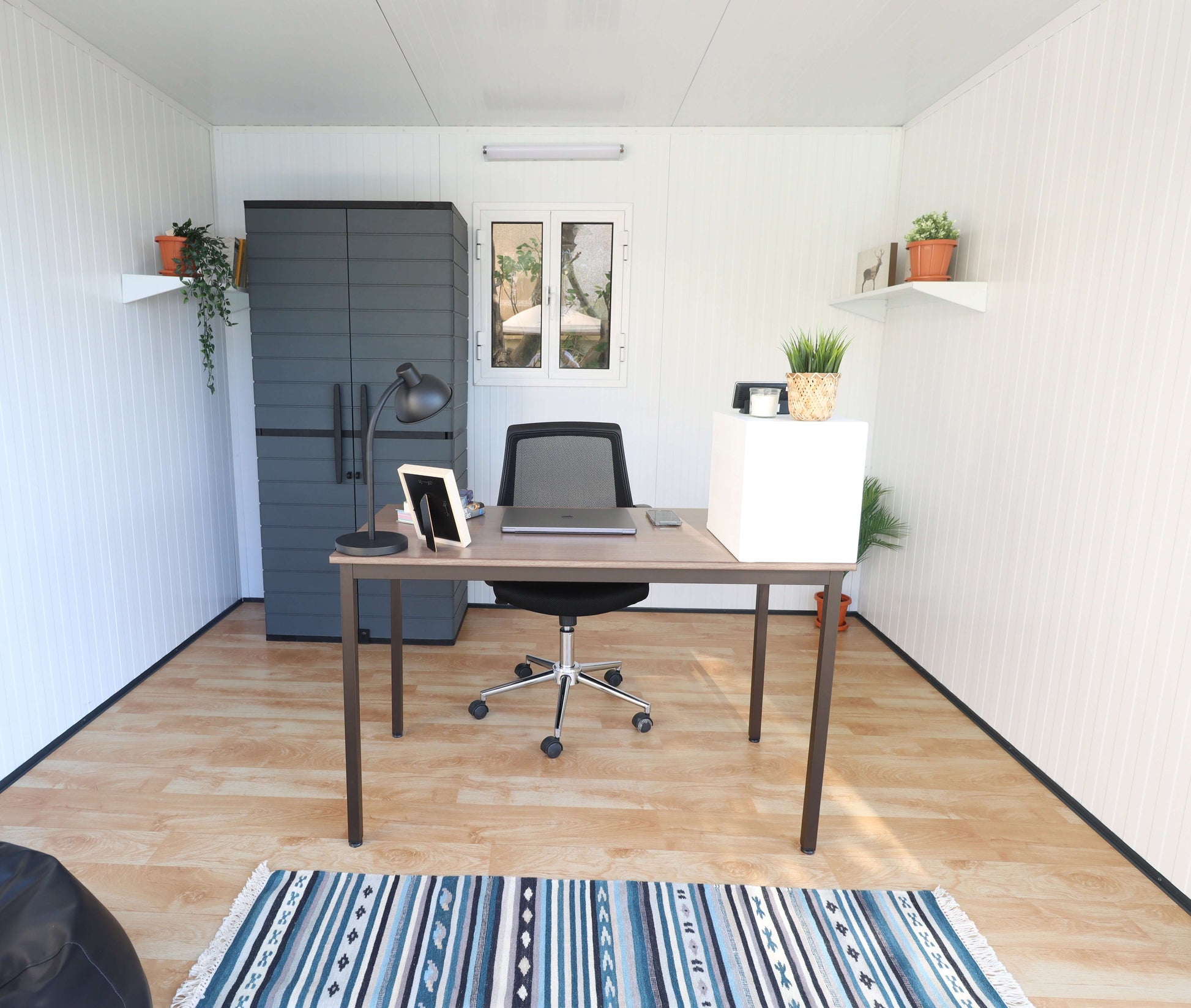 Interior of Duramax 10x10 Glass Garden Room with desk, chair, and plants, ideal as an office space. Features modern decor and ample lighting.