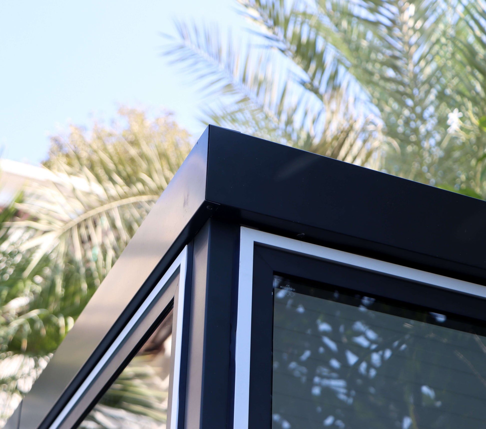 Close-up of Duramax 10x10 Glass Garden Room with sleek corner design, against a backdrop of palm trees.