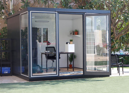 Duramax 10x10 Glass Garden Room 32001 with steel walls and clear panels, used as an office space in a backyard setting.