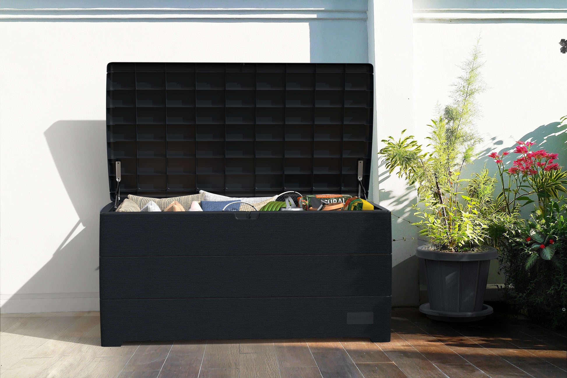 Duramax 110 Gal. Cedar Grain Deck Box in gray, open showing storage capabilities on a patio with plants beside it.