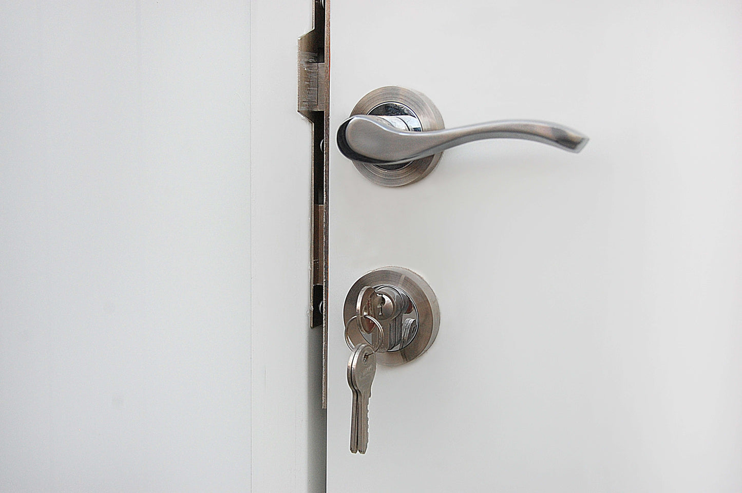 Modern silver door handle with a key in the lock on a white door, showcasing secure and stylish entry design.