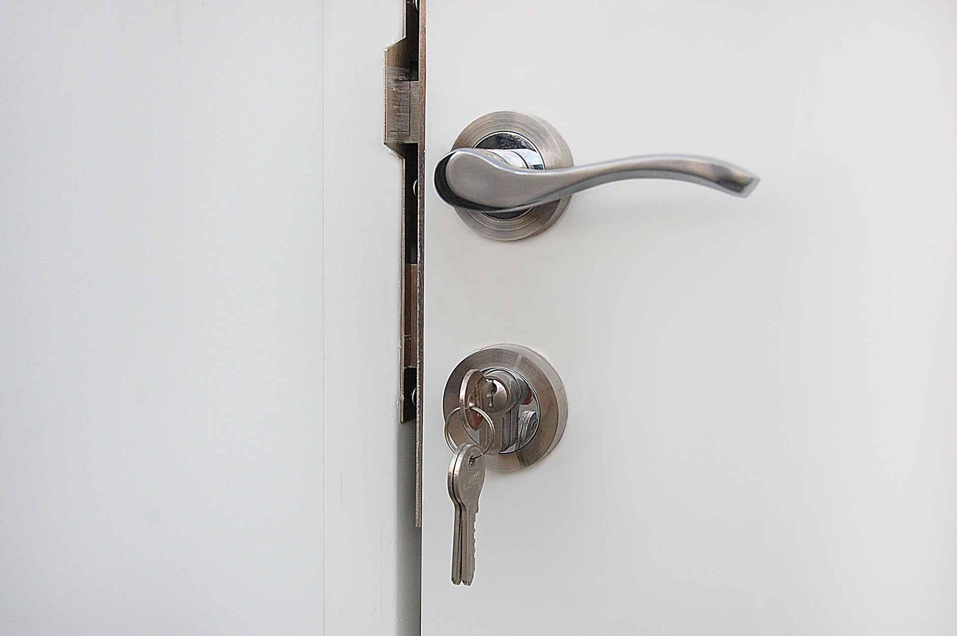 Modern silver door handle with a key in the lock on a white door, showcasing secure and stylish entry design.